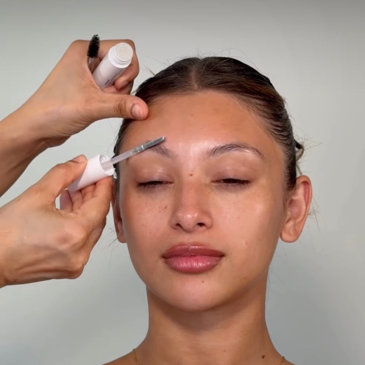 Makeup artist using KIMKO clear brow gel's dual-sided wand to sculpt laminated-look brows